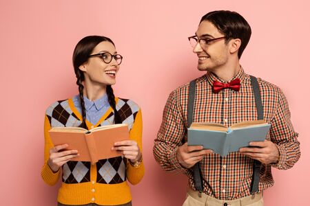 couple of smiling nerds in eyeglasses reading books on pink