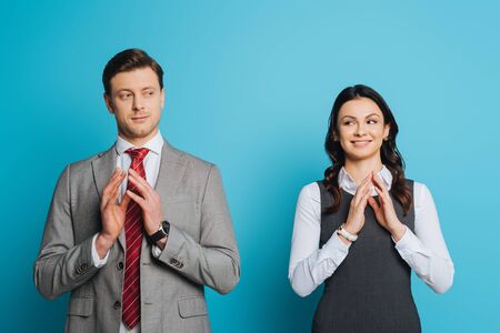 smiling, cunning businessman and businesswoman holding joined fingers on blue backgroundの写真素材