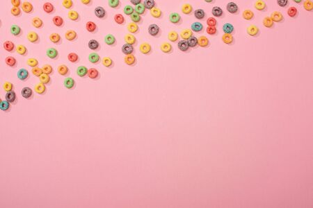 top view of bright colorful breakfast cereal scattered on pink background