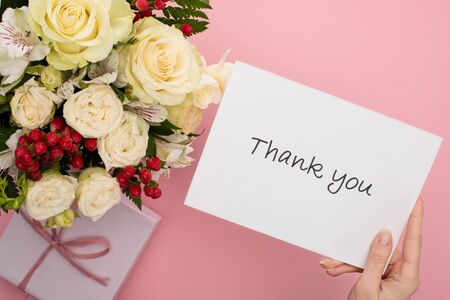 top view of bouquet of flowers near female hand with thank you card on pink backgroundの写真素材
