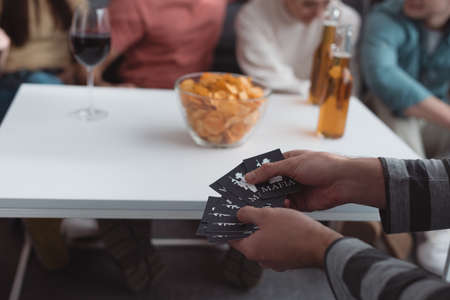 KYIV, UKRAINE - JANUARY 27, 2020: partial view of man holding mafia game cards near table with chips and drinksのeditorial素材