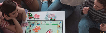 KYIV, UKRAINE - JANUARY 27, 2020: overhead view of smiling friends playing monopoly game, panoramic shotのeditorial素材