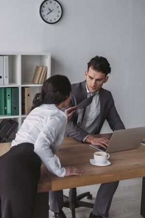 sensual secretary touching tie of handsome businessman while seducing him in officeの写真素材