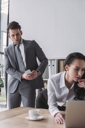 excited businessman taking picture of buttocks of secretary standing at workplaceの写真素材
