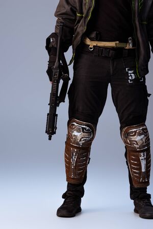cropped view of cyberpunk player holding gun and standing on grey