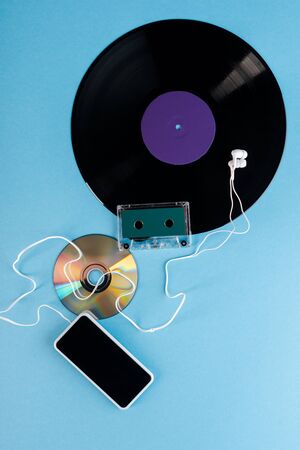 top view of vinyl record, compact disk, earphones, audio tape and smartphone with blank screen on...