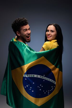 multicultural couple of smiling football fans with brazil flag on greyの写真素材