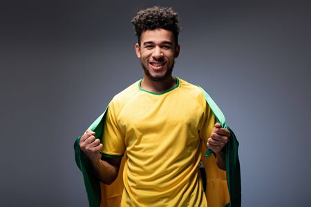 cheerful african american football fan holding brazilian flag on greyの写真素材