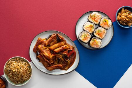top view of fresh tteokbokki  and gimbap near korean side dishes on white, blue and crimsonの写真素材