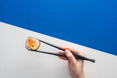 cropped view of woman holding chopsticks with korean gimbap on white and blueの写真素材