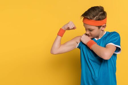 kid in sportswear showing muscles on yellow backgroundの写真素材