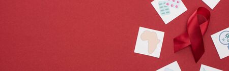 top view of red awareness aids ribbon and paper cards on red background, panoramic shot
