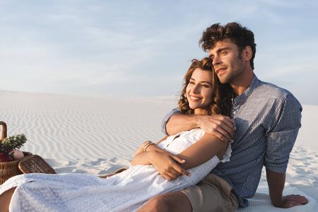 smiling young couple hugging while having picnic on beachの写真素材