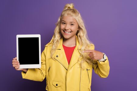smiling kid pointing with finger at digital tablet on purple backgroundの写真素材