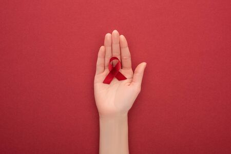 cropped view of woman holding red awareness aids ribbon on red background