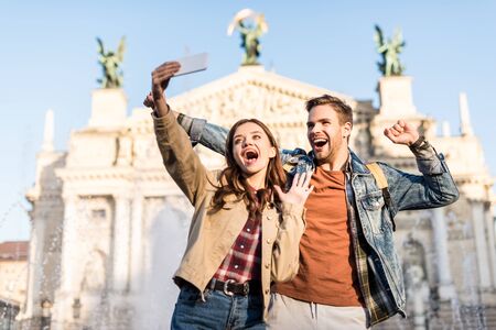 Excited couple taking selfie near fountain in cityの写真素材