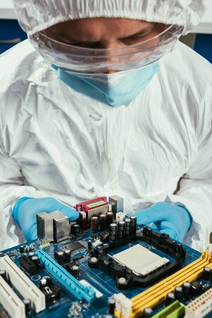 engineer in hazmat suit, medical mask and goggles holding motherboardの写真素材
