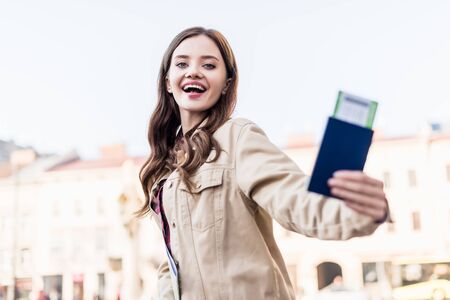 Low angle view of excited beautiful woman showing passport with air ticketの写真素材