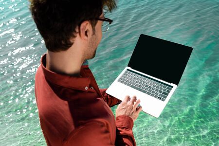 handsome freelancer with laptop standing in turquoise waterの写真素材