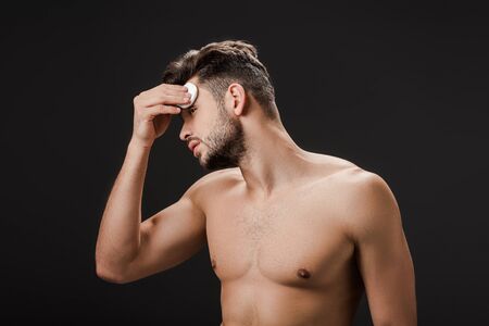 sexy naked man using cosmetic cotton pad isolated on blackの写真素材