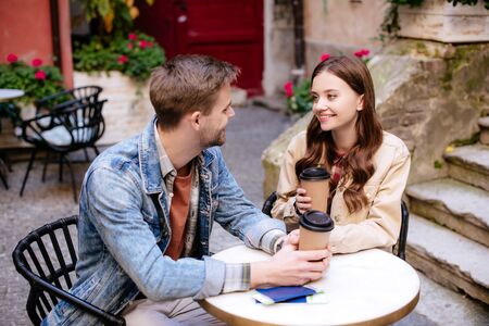 Selective focus of couple with disposable cups of coffee and passports looking at each other in cafe in cityの写真素材