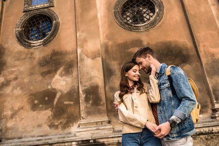 Low angle view of happy couple hugging and holding hands near wall