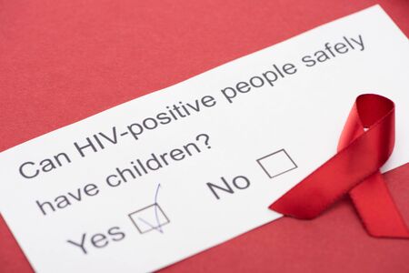 paper card with HIV questionnaire with awareness ribbon on red background