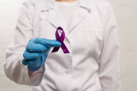 Selective focus of doctor holding purple ribbon on white backgroundの写真素材
