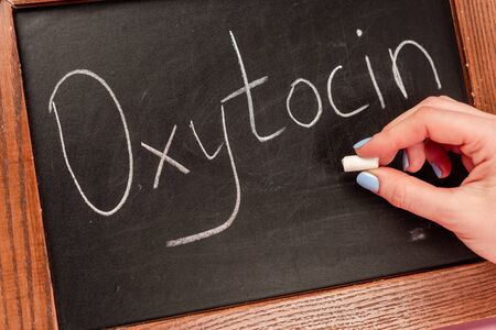 Cropped view of woman holding piece of chalk near blackboard with oxytocin lettering