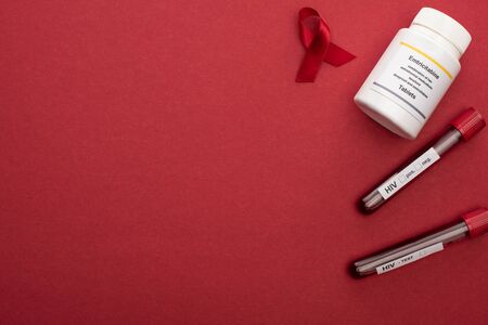 top view of red awareness aids ribbon, emtricitabine pills and test tubes with blood samples on red...