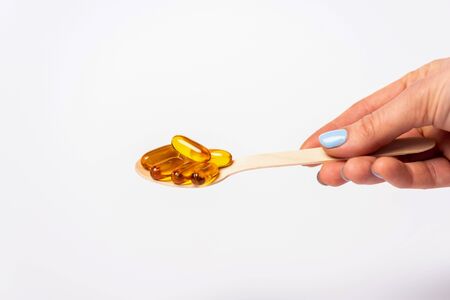 Cropped view of woman holding wooden spoon with pills of omega 3 isolated on whiteの写真素材