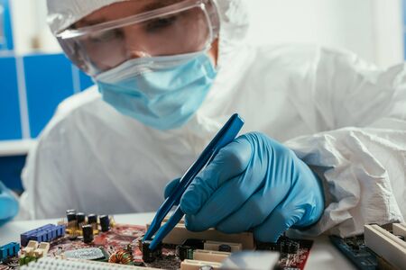 engineer in medical mask and goggles fixing computer motherboard with tweezersの写真素材