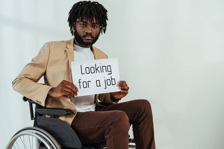 Disabled african american man with placard with looking for a job lettering on wheelchair on whiteの写真素材