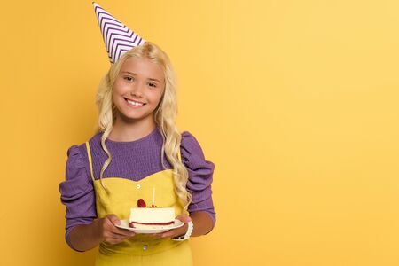 smiling kid holding plate with birthday cake on yellow backgroundの写真素材