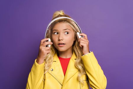 excited kid with headphones looking away on purple backgroundの写真素材