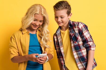 smiling and cute kids using smartphone on yellow background