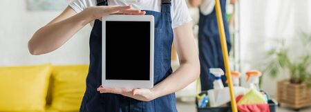 panoramic shot of cleaner in uniform holding digital tablet with blank screenの写真素材