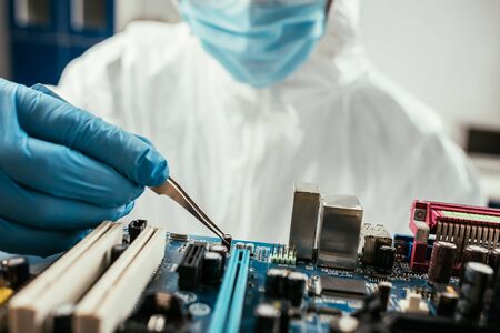 cropped view of engineer holding tweezers near computer motherboad