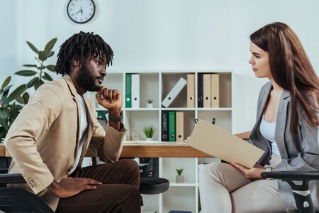 Disabled african american employee and recruiter with folder looking at each other at job interview in officeの写真素材