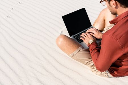 freelancer sitting on sandy beach with laptop against clear blue skyの写真素材
