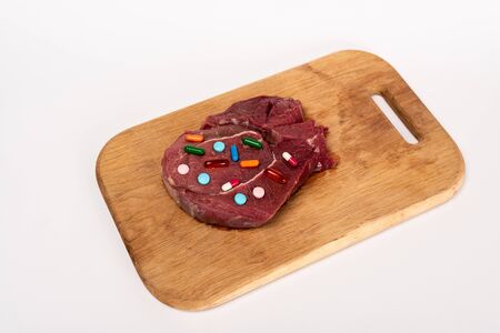 High angle view of hormonal pills on piece of raw meat on cutting board isolated on white