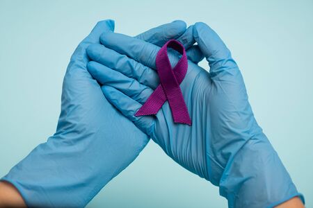 Cropped view of doctor in latex gloves holding purple ribbon isolated on blue