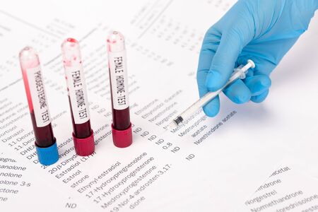 Cropped view of doctor holding syringe near test tubes with blood samples and lists with hormones