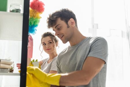 selective focus of attractive girl looking at happy man cleaning rack at home