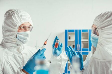 biochemist holding syringe and container with medicine near colleague in lab