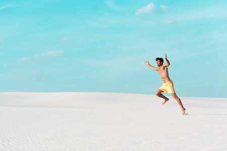 man in swim shorts with muscular torso running on sandy beachの写真素材
