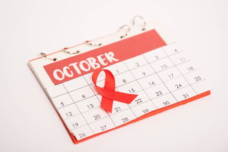 Selective focus of red ribbon of aids awareness on calendar of october isolated on whiteの写真素材
