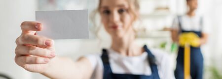 panoramic shot of attractive cleaner in uniform holding blank cardの写真素材