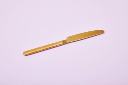 metal shiny golden knife on violet background