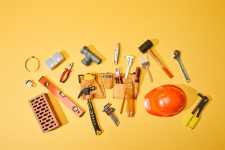 top view of tool belt, brick, industrial tools and helmet on yellow backgroundの写真素材